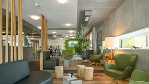Ein modernes Interieur mit einem grünen Sofa, Holzelementen und einem grünen Sessel am Fenster.