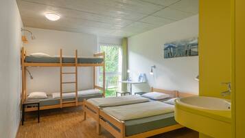 A dormitory room with bunk beds, a desk, a chair, and a bathroom with a sink.
