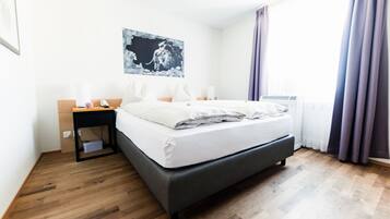 Ein modernes Hotelzimmer mit einem großen Bett, einem Nachttisch mit Lampe, einem Bild an der Wand und einem Fenster mit Vorhängen.