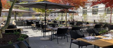 An outdoor patio area with tables and chairs, umbrellas, and potted plants.