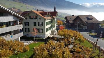 Ein mehrstöckiges Gebäude mit einem Balkon, einer Treppe, die zum Eingang führt, und einer Bergkette im Hintergrund.