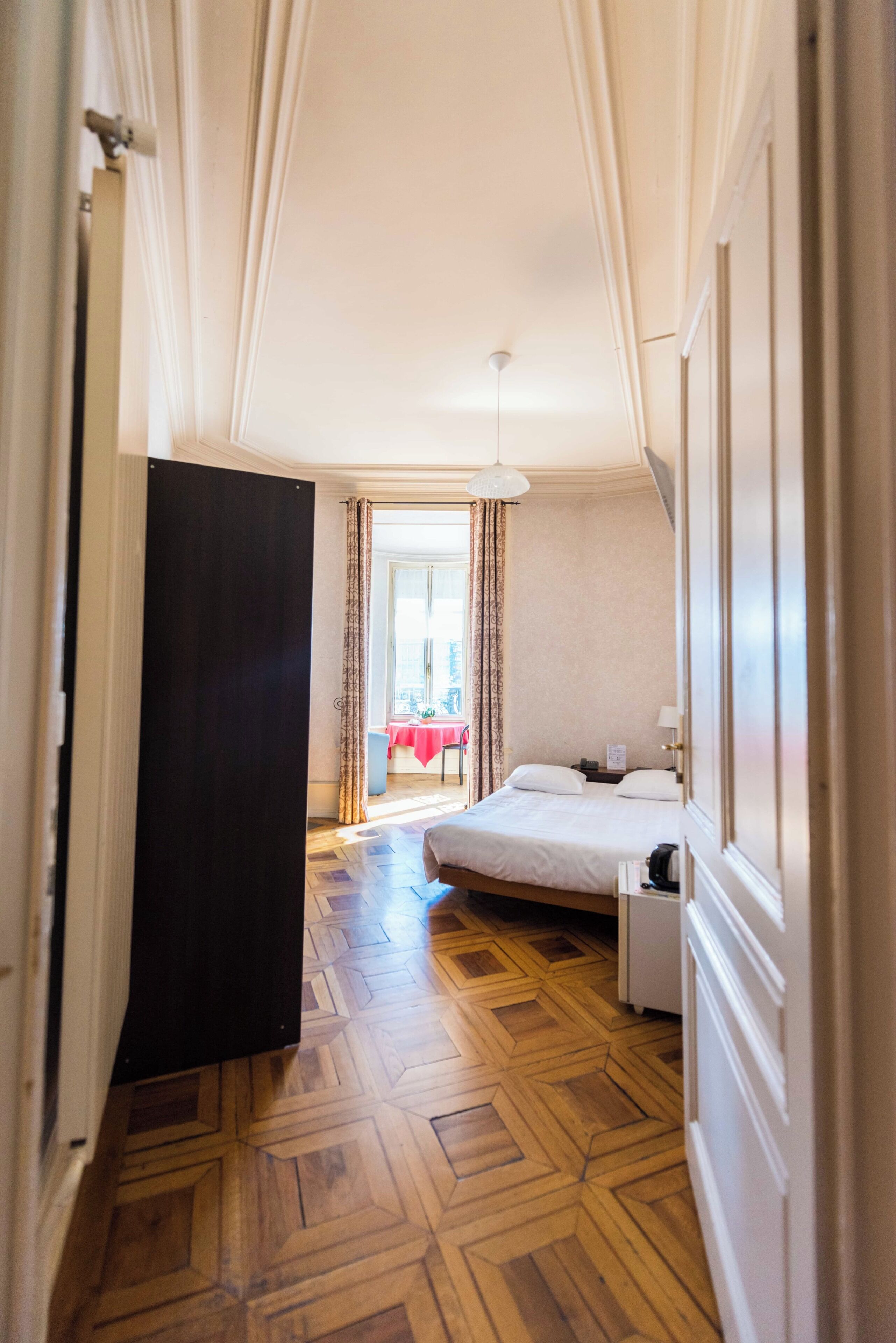 A hotel room with a bed, a nightstand, a door, and a view of a dining area.
