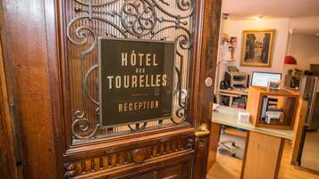 A wooden reception desk with a sign for "Hôtel des Tourelles" and a computer setup in the background.