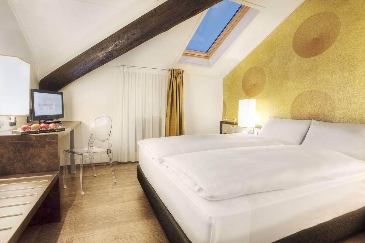 A hotel room with a bed, desk, chair, and a skylight.