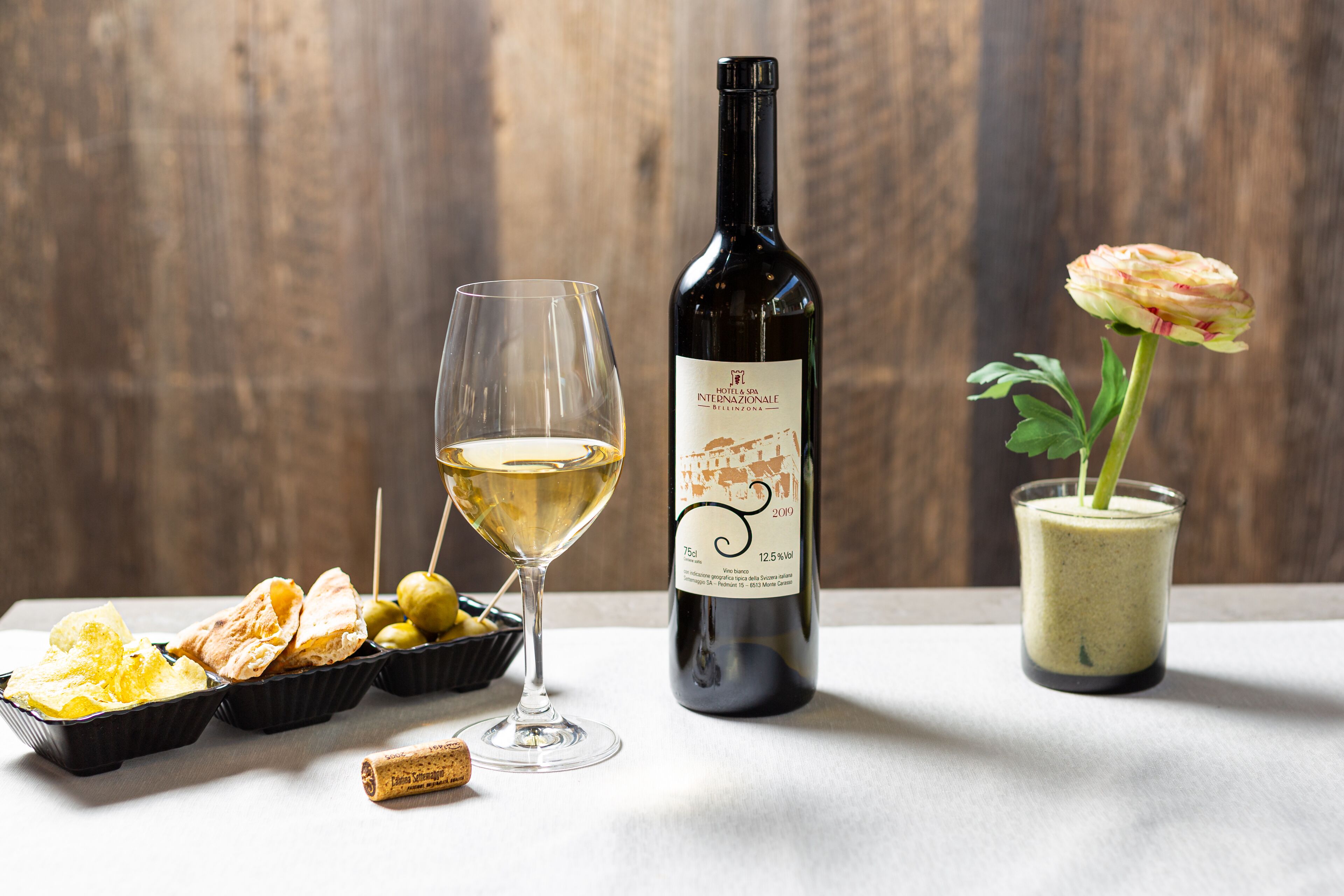 Une bouteille de vin, un verre de vin, une fleur et des amuse-gueules sur une table.