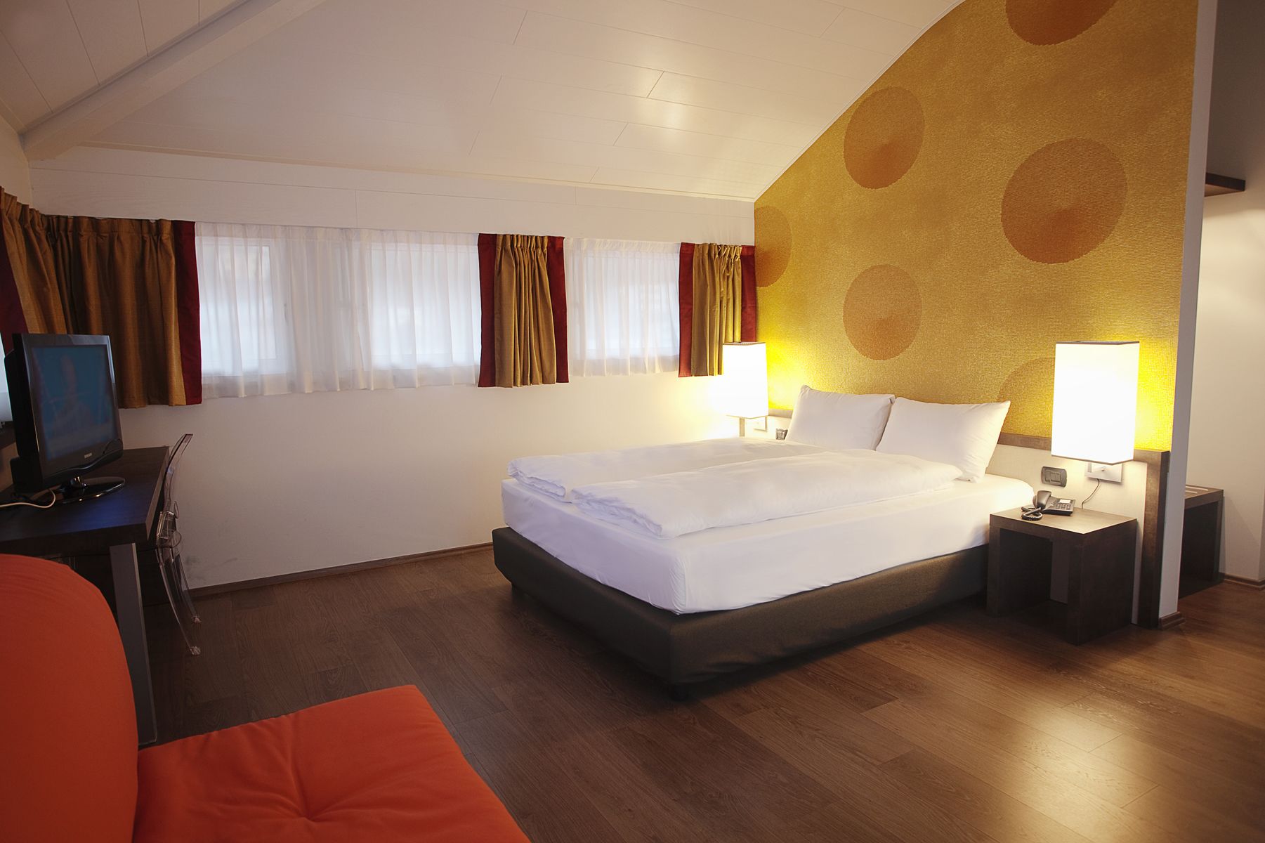 A hotel room with a bed, a desk with a computer, and a chair.