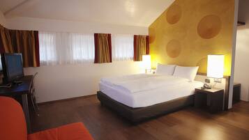 A hotel room with a bed, a desk with a computer, and a chair.
