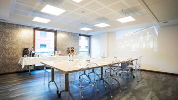 A conference room with a long table, clear chairs, a projector screen, and a patterned wall.