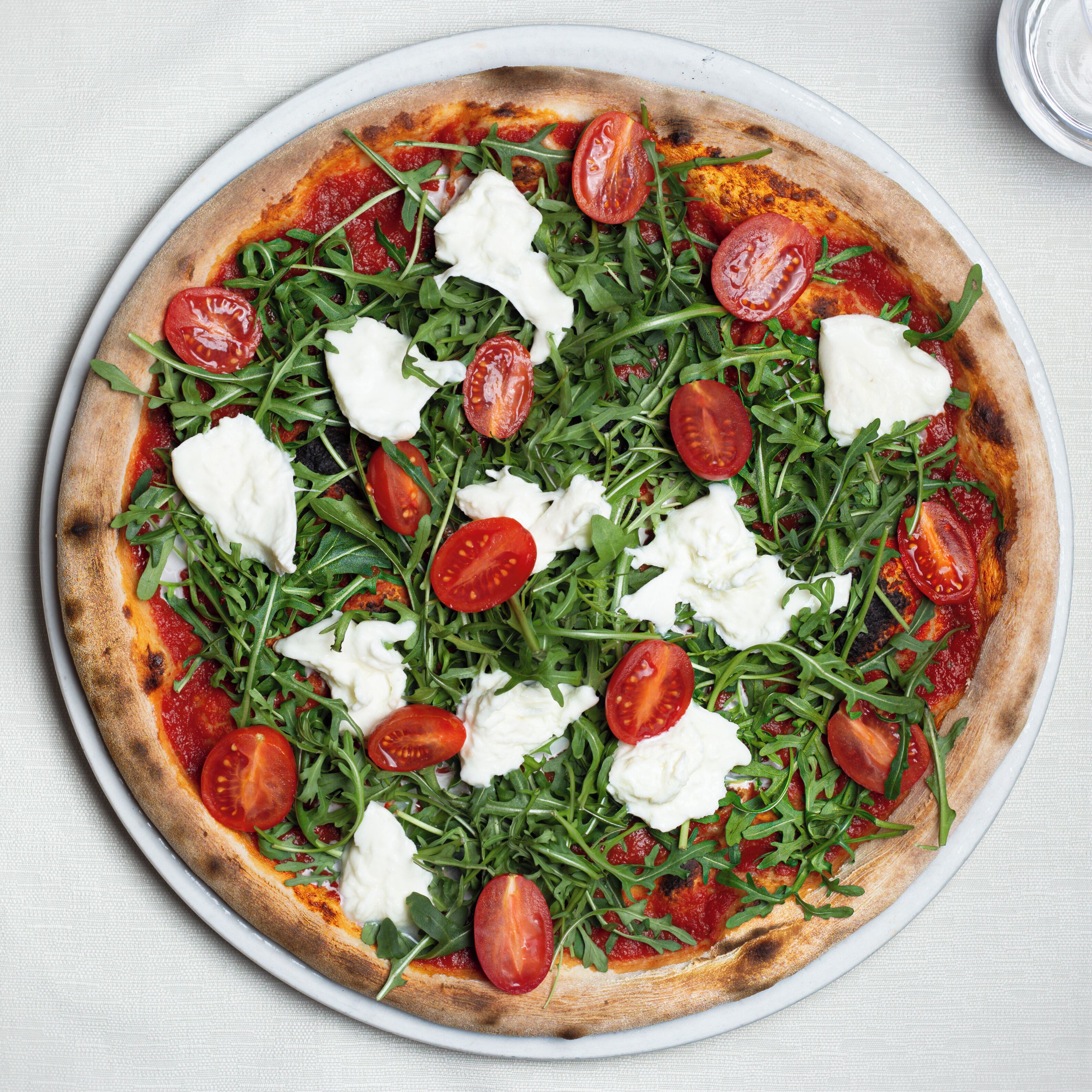 A pizza with tomato sauce, mozzarella cheese, and arugula on a white plate.