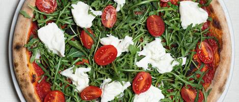 A pizza with tomato sauce, mozzarella cheese, and arugula on a white plate.