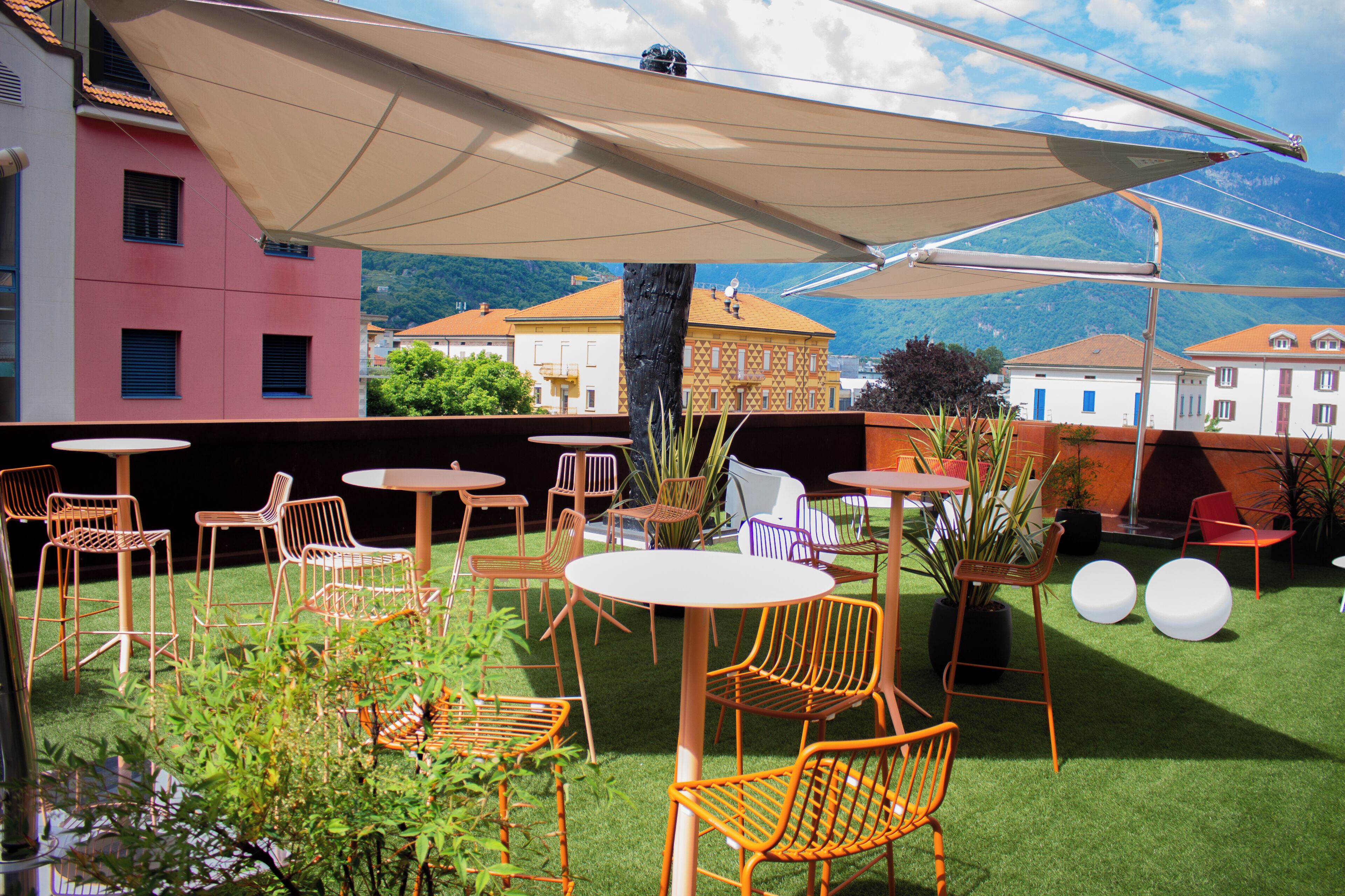 An outdoor seating area with tables and chairs, surrounded by buildings and a mountain view.