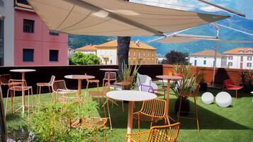 An outdoor seating area with tables and chairs, surrounded by buildings and a mountain view.
