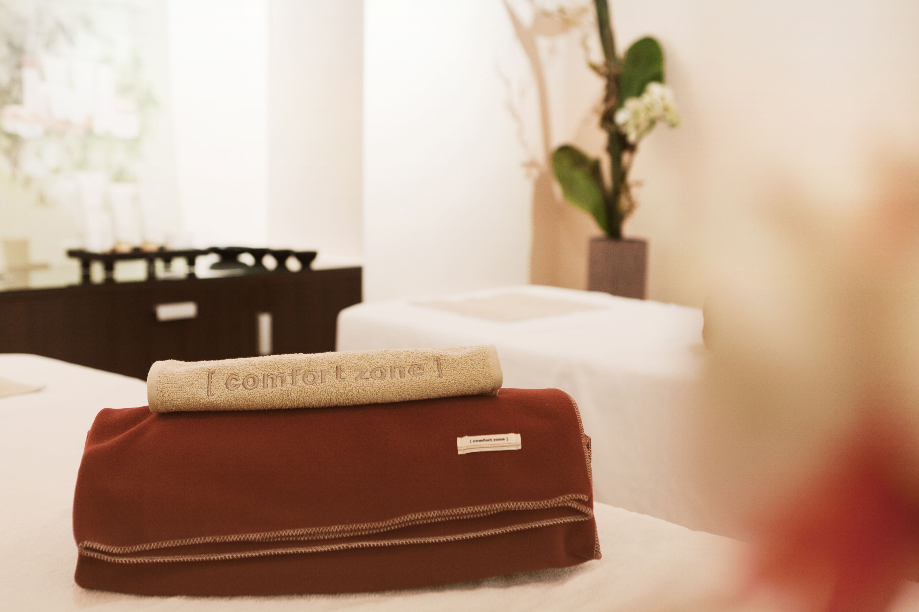 Cama arrumada com uma toalha dobrada e uma pequena bolsa sobre ela.