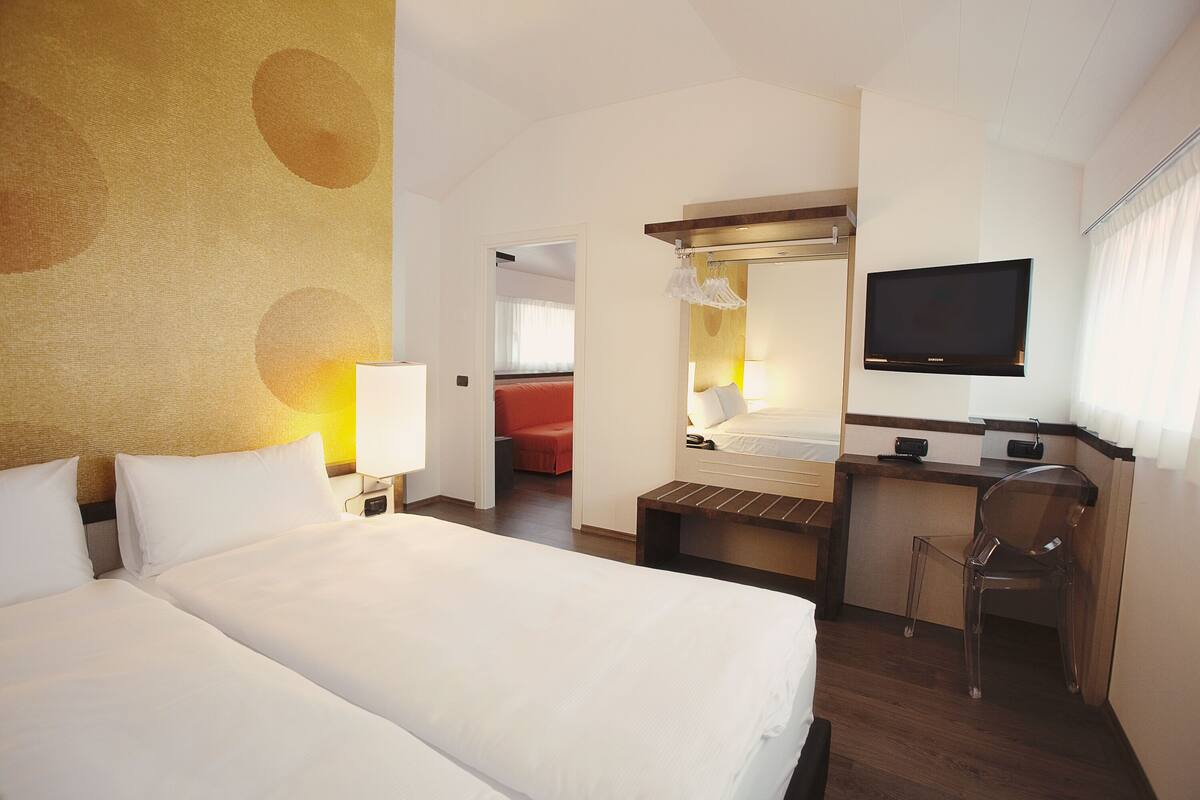 A hotel room with two beds, a desk, a chair, a television, and a bathroom visible through an open door.