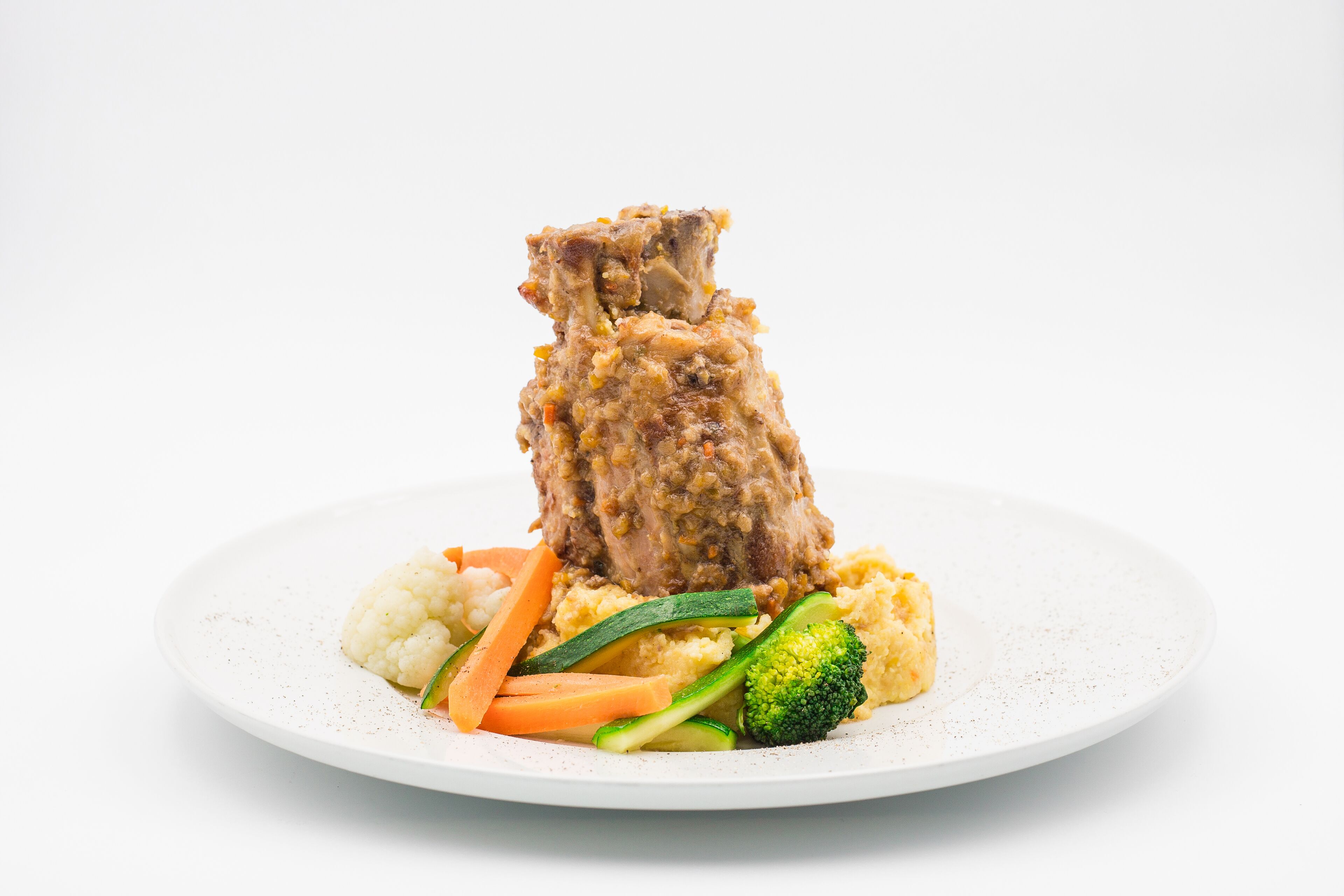 A plate with a piece of meat, cauliflower, carrots, zucchini, and broccoli.
