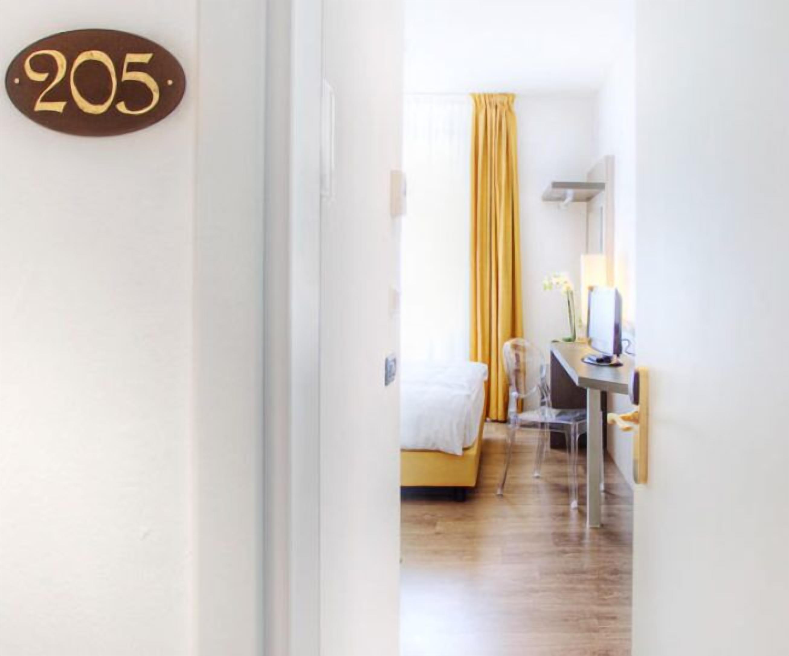 A hotel room with a bed, a desk, a chair, and a yellow curtain.
