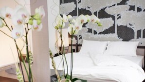 A neatly made bed with white linens, a headboard with a patterned design, and white orchids in a vase.
