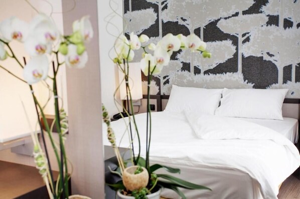 A neatly made bed with white linens, a headboard with a patterned design, and white orchids in a vase.