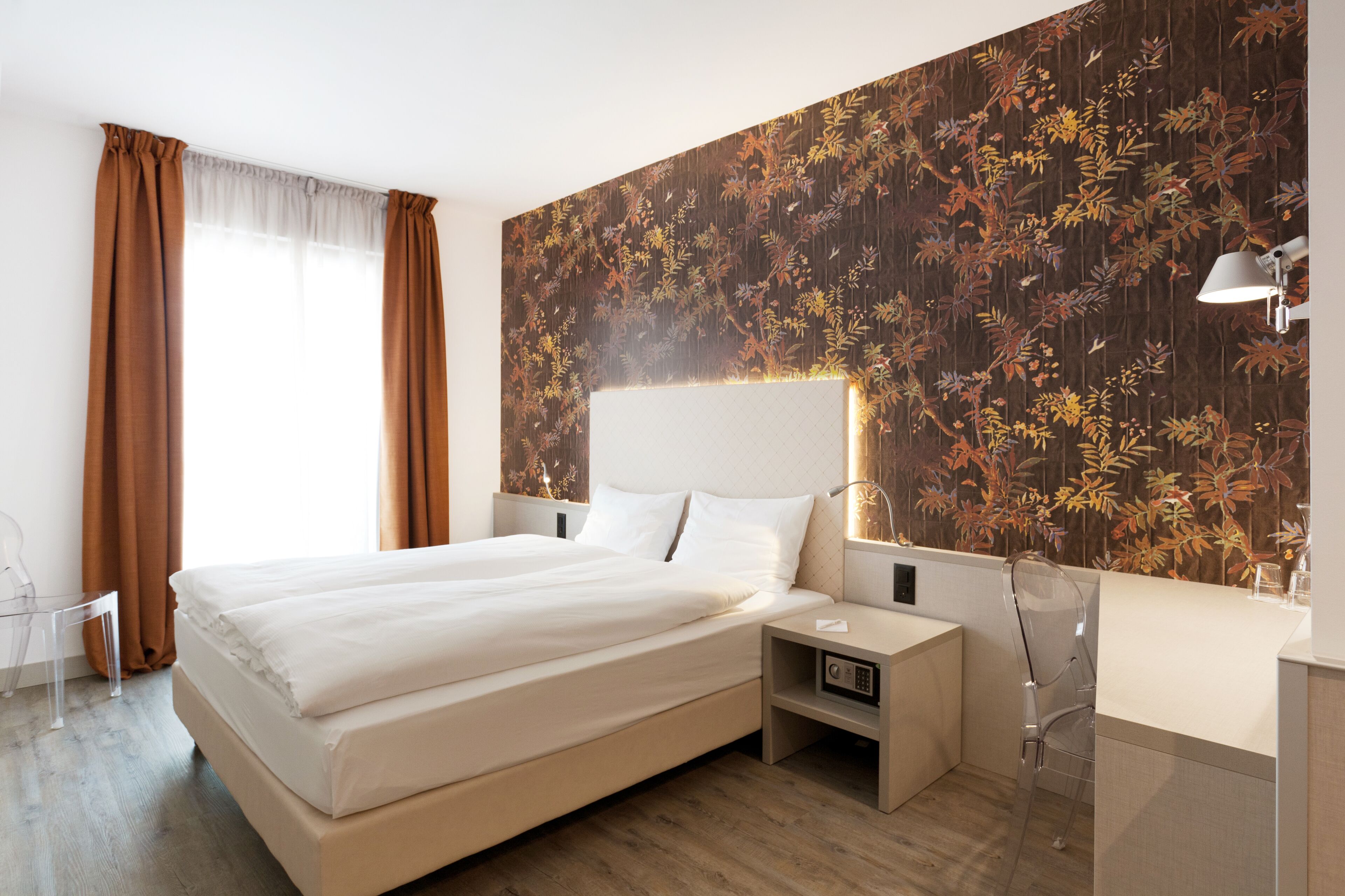 A modern hotel room with a large bed, a nightstand, a desk, and a chair.