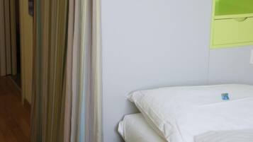 Una habitación de hotel con una cama, un estante verde en la pared con un objeto blanco y una cortina a rayas.
