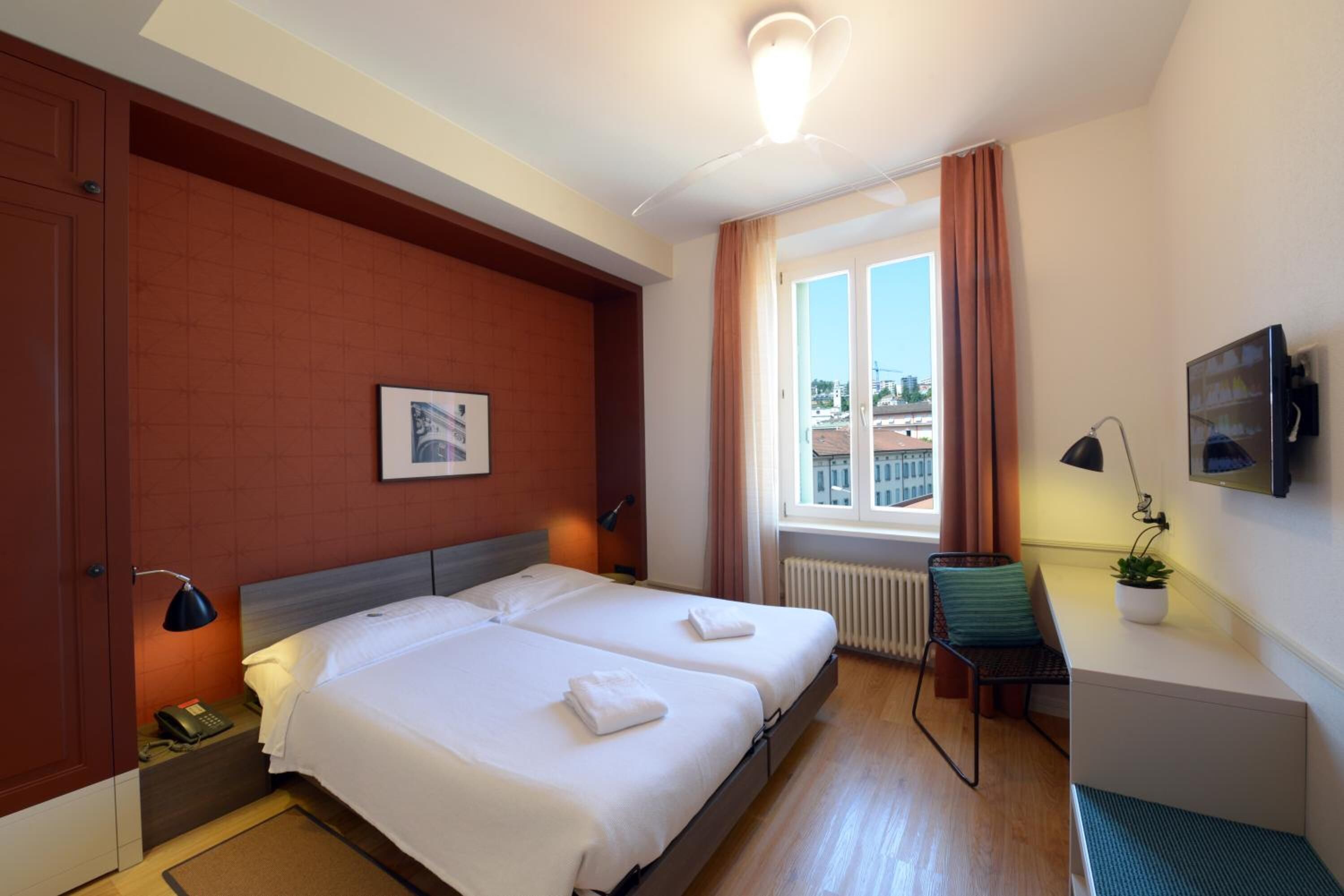 A hotel room with two beds, a desk, a chair, a TV, and a window with curtains.