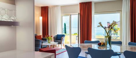 A modern hotel room with a balcony, a dining area with blue chairs, and a table with a vase of flowers.