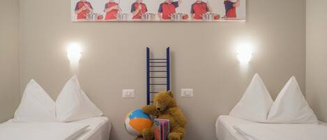 Un dormitorio con dos camas, un oso de peluche en una silla, una pelota de playa y un cuadro de cocineros en la pared.