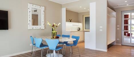 A modern dining area with a round table and blue chairs, a decorative mirror, and a kitchen in the background.