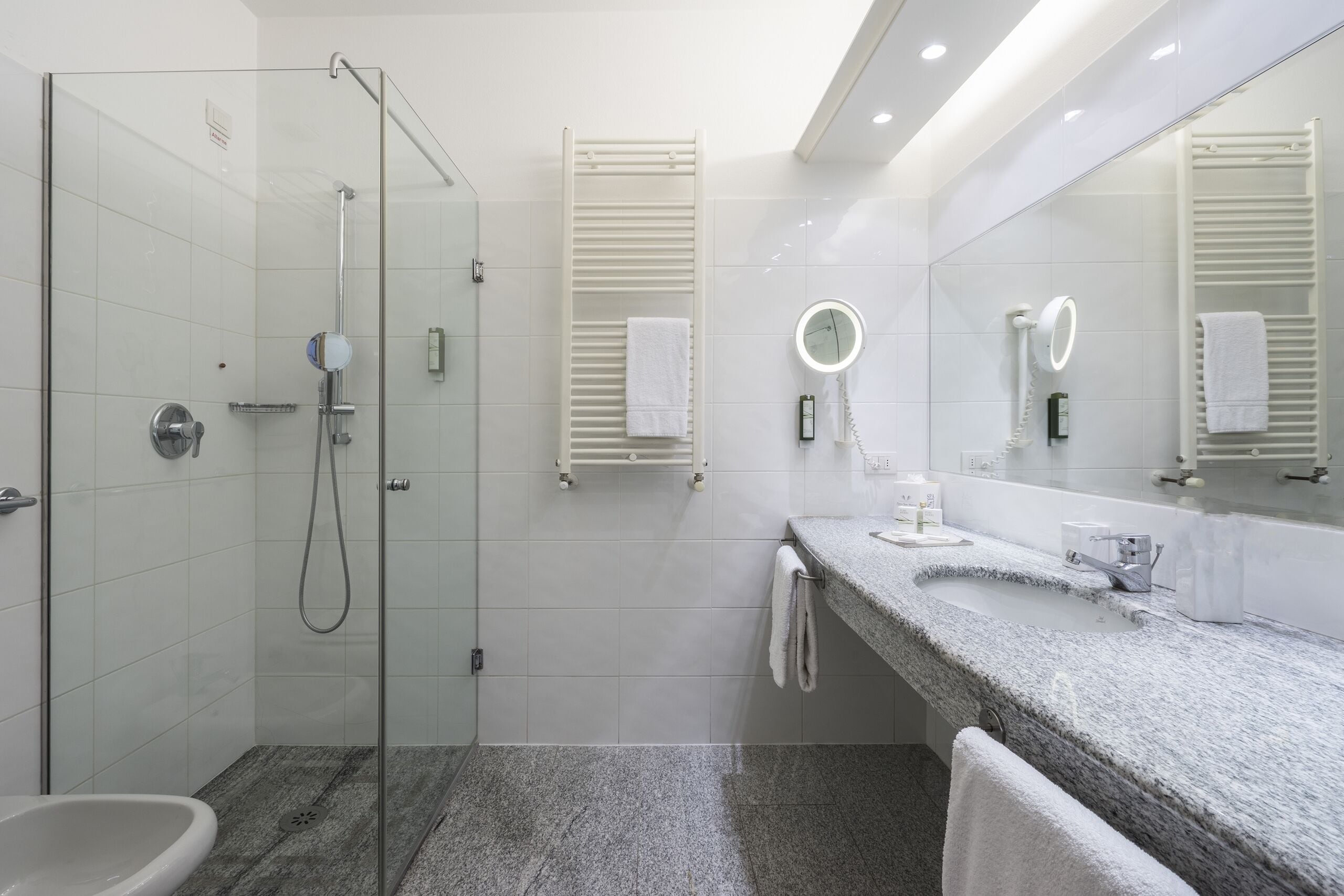 Un baño moderno con cabina de ducha de vidrio, lavamanos con encimera de granito y un espejo grande con iluminación.