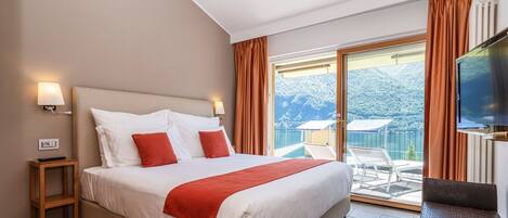 Een hotelkamer met een groot bed, een televisie, een tafeltje en een balkon met uitzicht op de bergen.