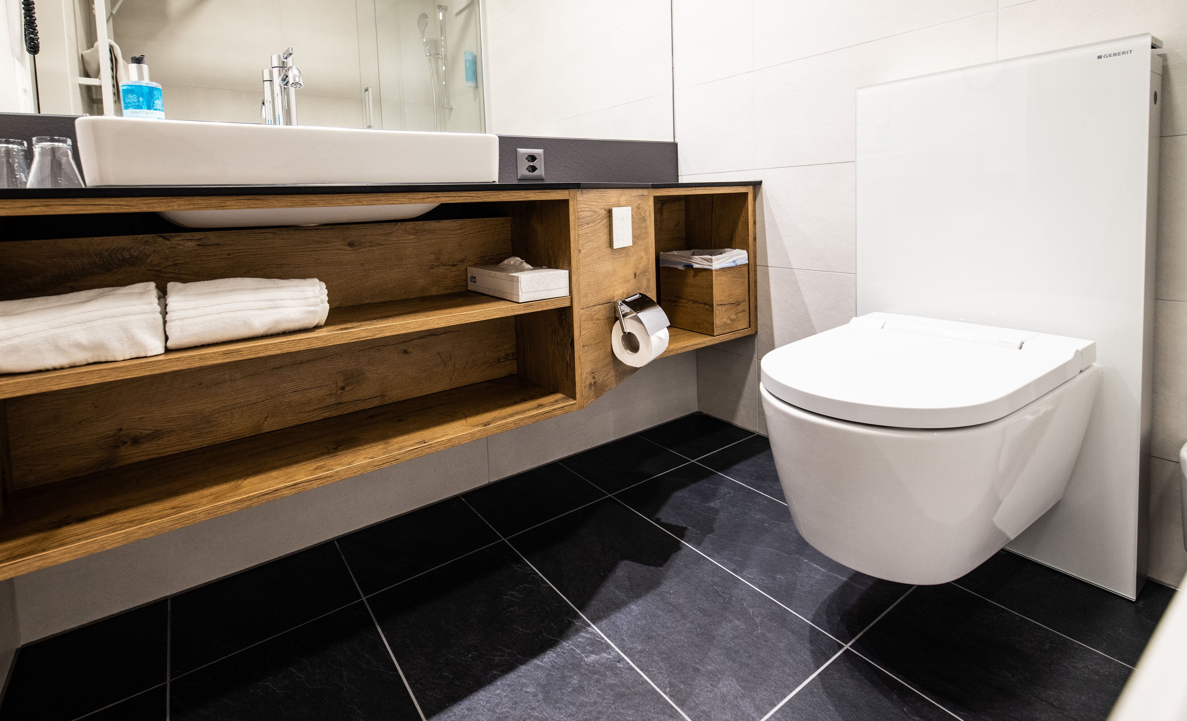 Un baño moderno con tocador de madera, un lavabo blanco y un inodoro.