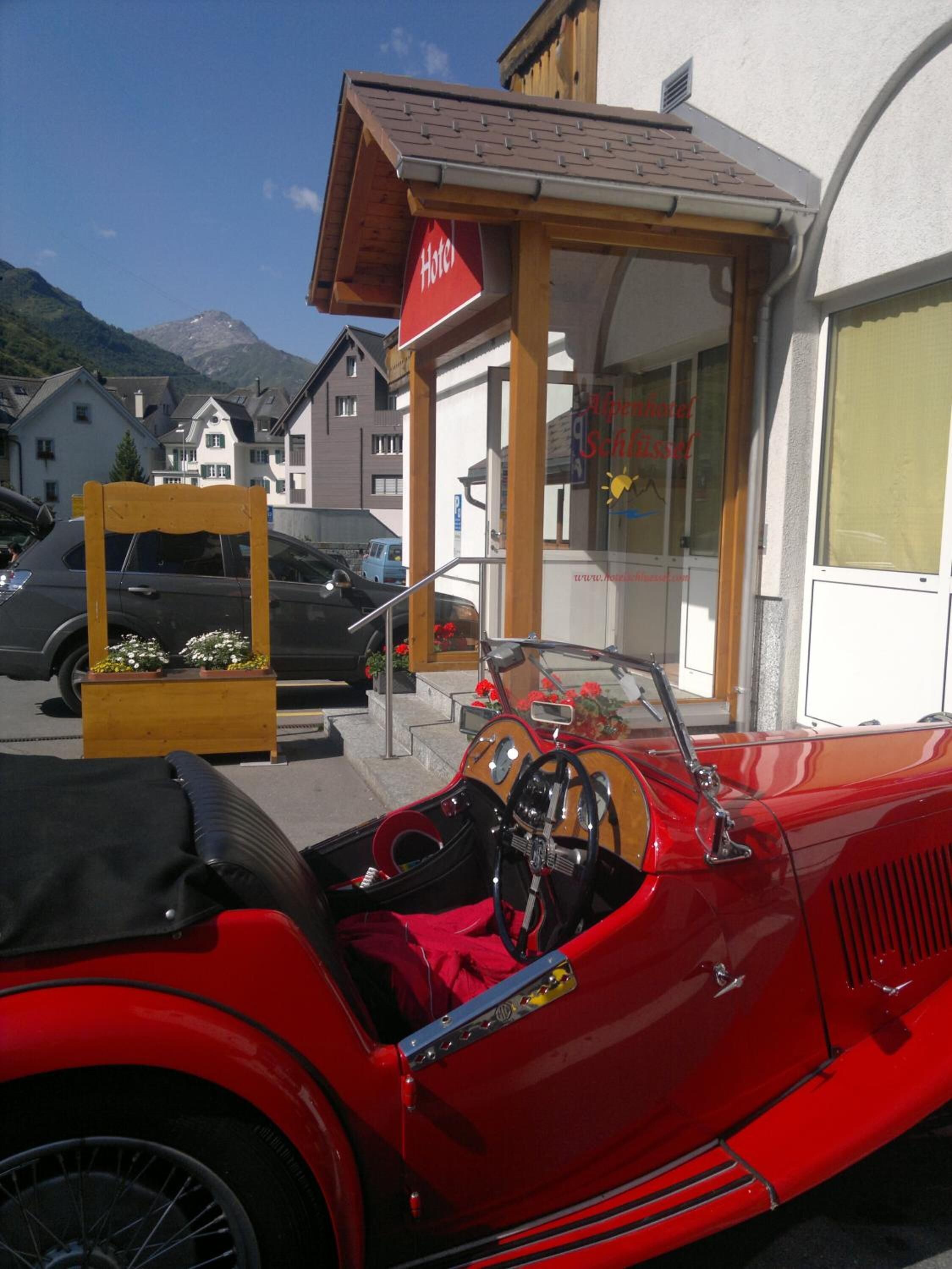A red vintage car parked in front of a hotel with a wooden facade and a sign that reads "Hotel".