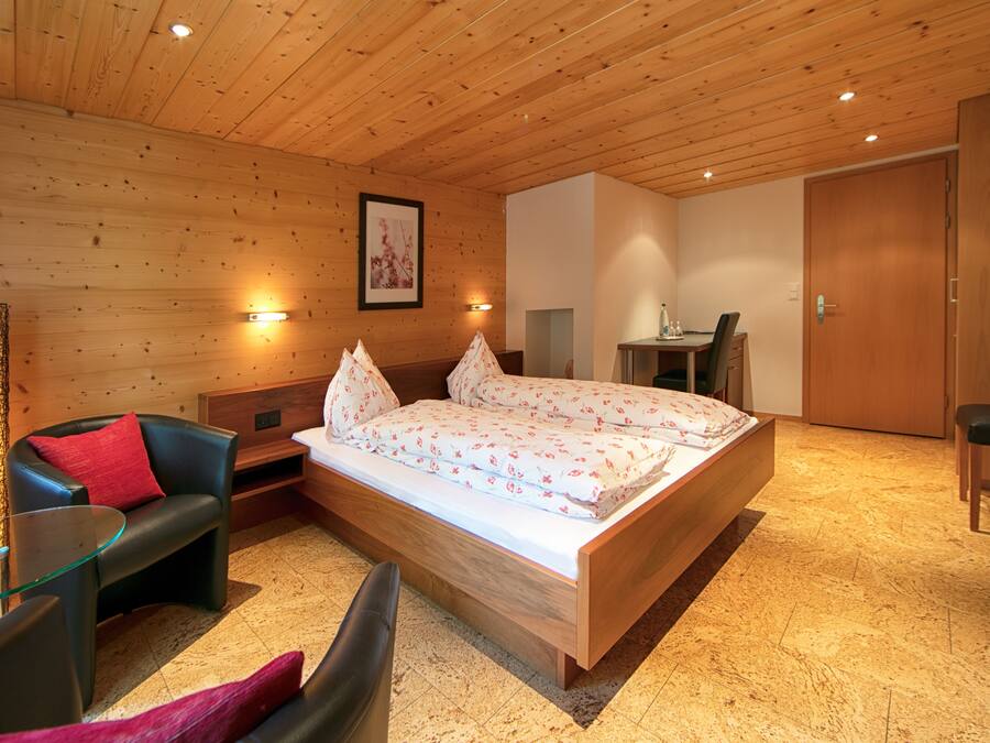 A wooden-paneled room with a bed, a sofa, a small table, and a chair.