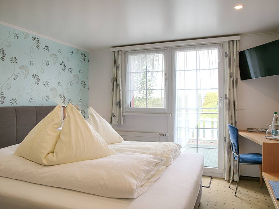 Ein Hotelzimmer mit Bett, Schreibtisch, Stuhl, Fernseher und einem Fenster mit Vorhängen.