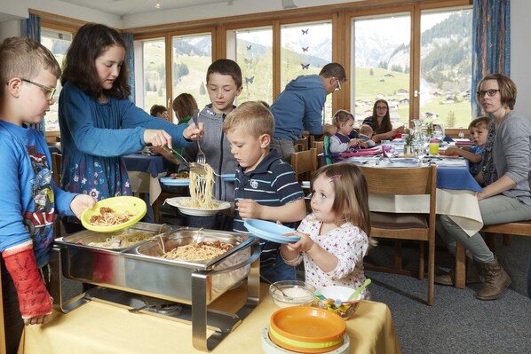 Una familia cenando en un espacio amplio con ventanas grandes, una mesa de buffet y mobiliario de madera.