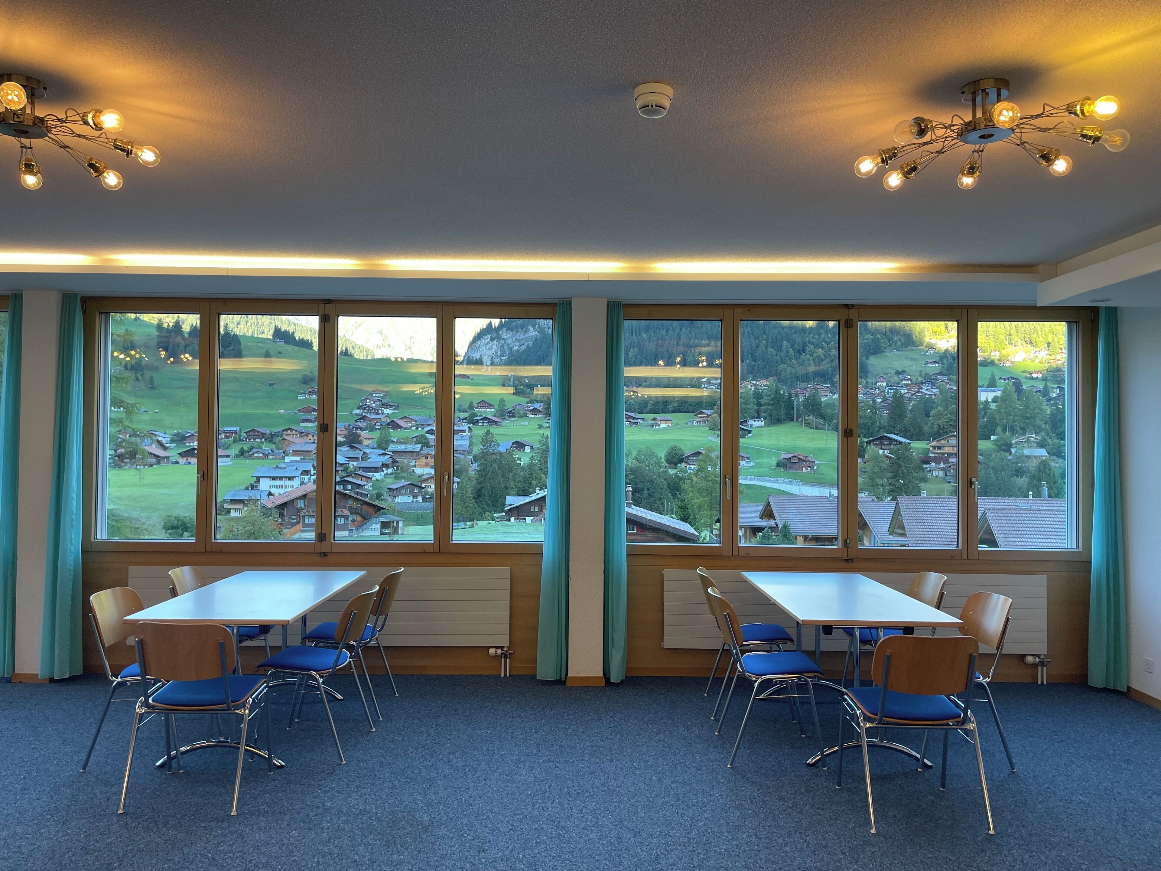 Un salón de conferencias con amplios ventanales, una mesa, sillas e iluminación en el techo.