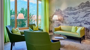A room with a green sofa, two armchairs, a coffee table, and a mountain mural on the wall. - Ferien- und Familienhotel Alpina (Adelboden)