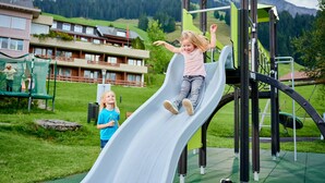 A playground with a slide, surrounded by green grass and buildings. - Ferien- und Familienhotel Alpina (Adelboden)