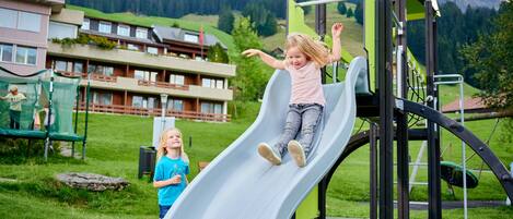 A playground with a slide, surrounded by green grass and buildings.