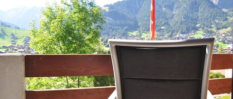 Un balcon donnant sur un paysage montagneux, avec une balustrade en bois et une chaise.