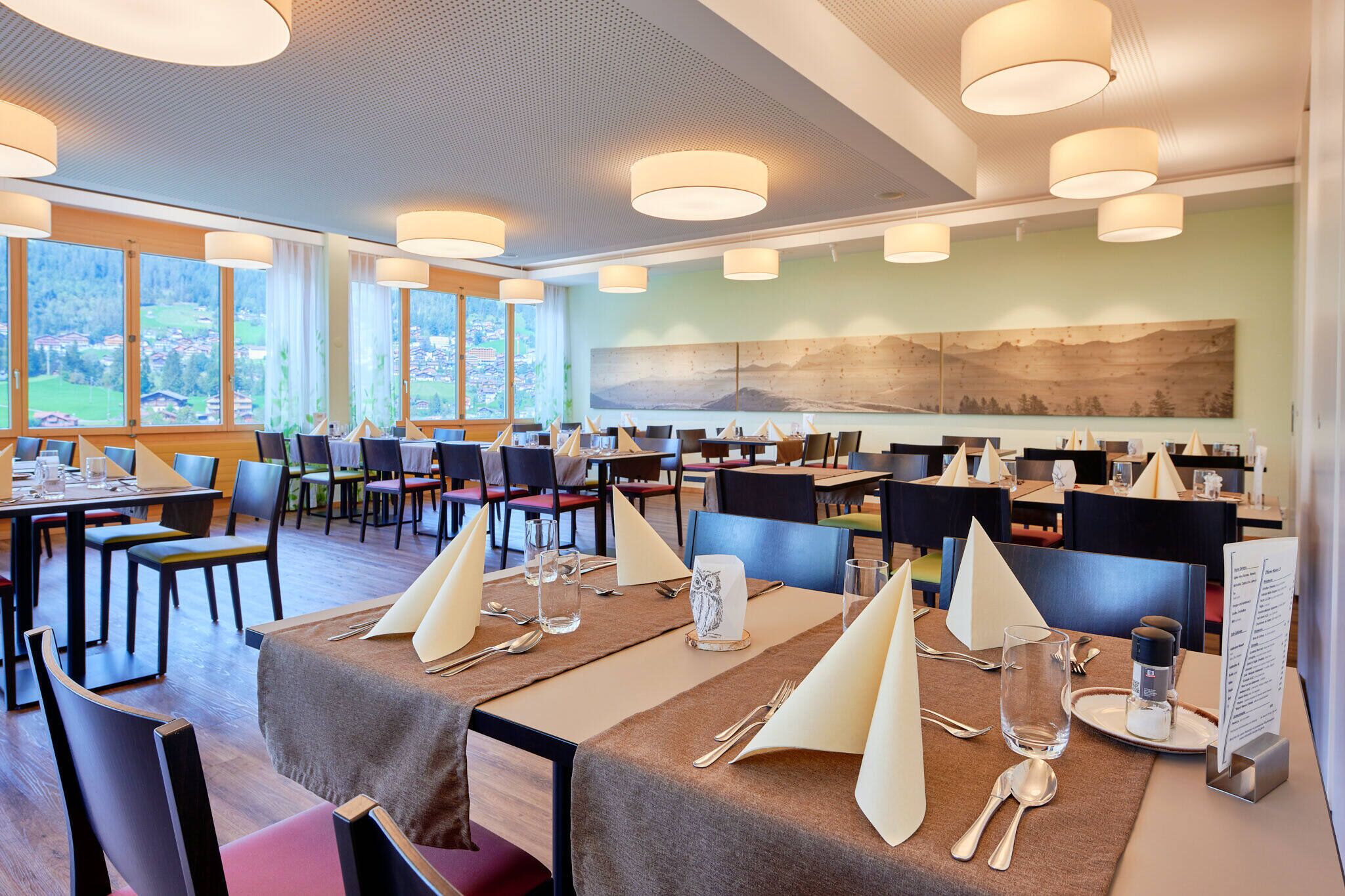 Un espace repas avec des tables dressées, de grandes fenêtres et une vue sur l’extérieur.