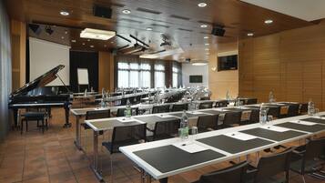 Une salle de conférence équipée d’un piano, de longues tables, de chaises et d’un écran de projection.