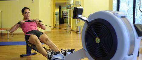 A person using a rowing machine in a gym with wooden floors and yellow walls.