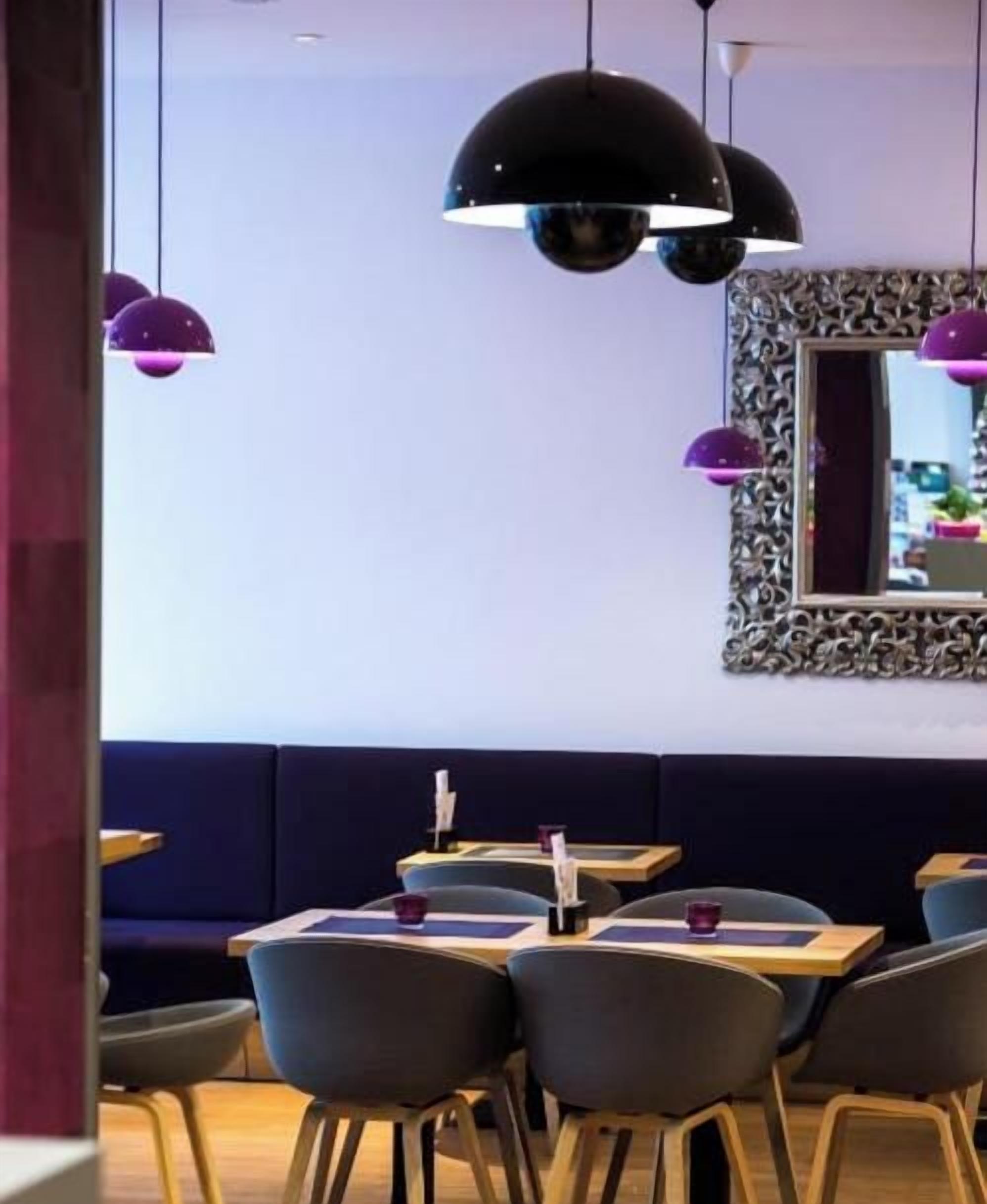 A restaurant interior with round tables, dark seating, and pendant lighting.