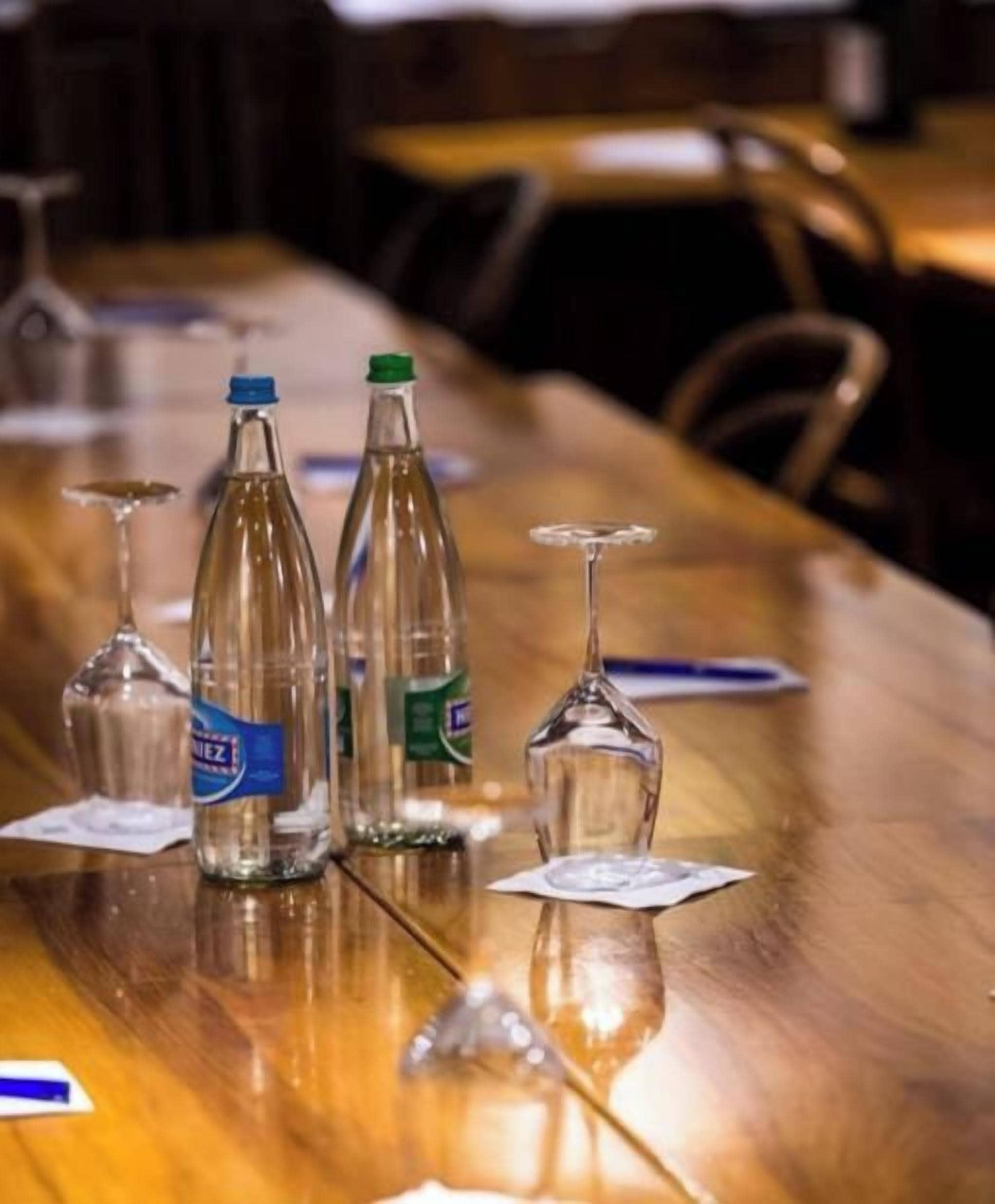 Una mesa de madera con botellas de vidrio transparente y copas de vino.