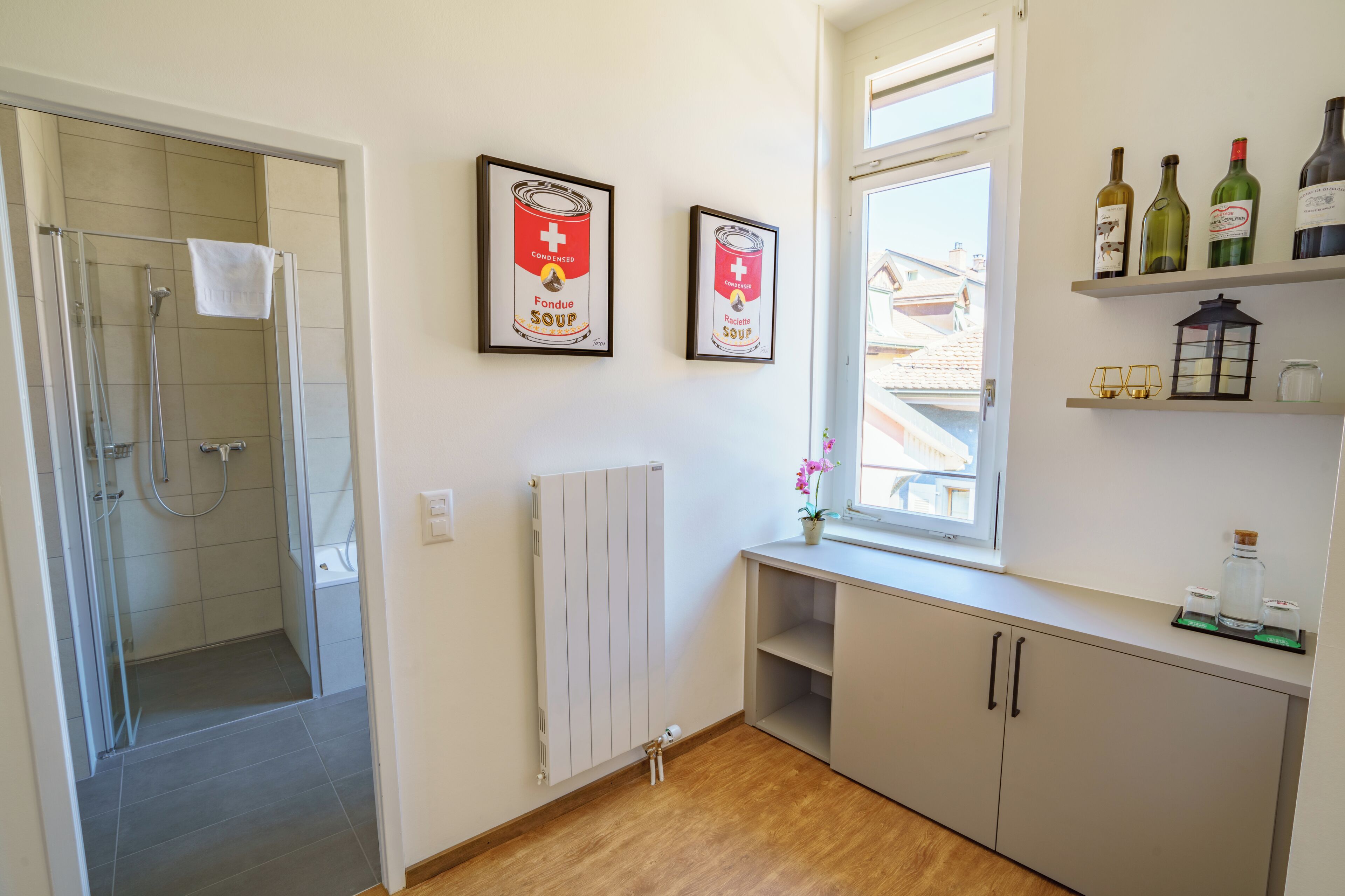Un baño moderno con cabina de ducha de vidrio, radiador blanco y ventana con vista a edificios.