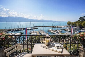 A table with a wine glass, a bottle, and an open book, overlooking a marina with boats and mountains in the background. - Rivage Hotel Restaurant Lutry (Lutry)