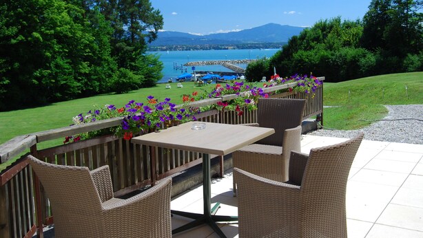 An outdoor patio with wicker furniture, a table, and a flower arrangement. - Hotel La Barcarolle (Prangins)
