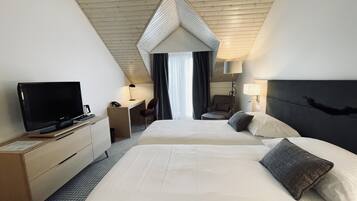 Habitación de hotel con dos camas, un escritorio, una silla, un televisor y una lámpara.