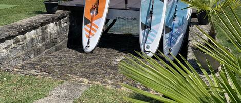 Three surfboards leaning against a railing by a lake with mountains in the background.